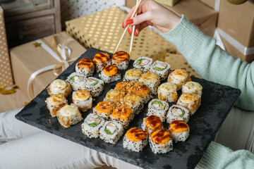 Sushi sticks in the hands of a woman against a set of sushi on a slate. Oriental cuisine. 45 view