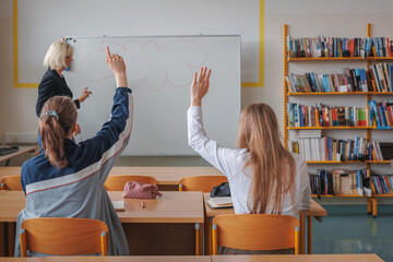Two girl students during a classroom lecture, listening and communicating with a teacher. Education and learning concept.
