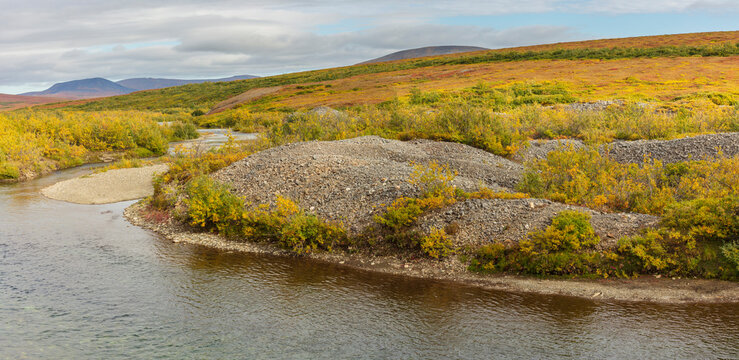 Tundra landscape in Western Alaska with rolling hills piles of mine tailings left behind by a gold dredge and river in autumn colors in the vicinity of Nome, Alaska
