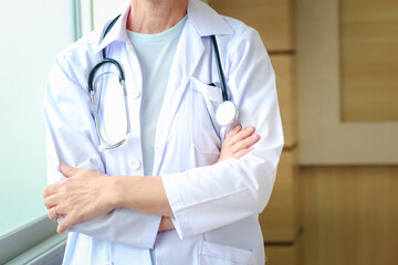 Confident female doctor in white workwear with stethoscope, standing with arms crossed in clinic hospital. Professional senior woman doctor at medical workplace.