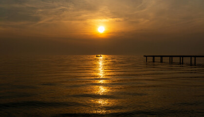 Obraz premium The sunset and the pier, the red of which is reflected in the sea.