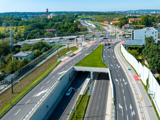 City highway in Krakow, called Trasa Lagiewnicka with multilane road with tunnels, junctions for cars and trams, bicycle lanes, walkways with zebra crossings and acoustic screens. Aerial view - 645705883
