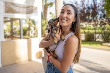 Cute young woman is kissing and hugging her little dachshund puppy. Love between owner and dog. Outdoor photo in the park, selective focus. Lifestyle concept.