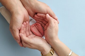 The palms of the father, the mother are holding the foot of the newborn baby on blue background. Feet of the newborn on the palms of the parents. Photography of a child's toes, heels and feet