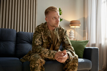 Depressed veteran wearing military uniform sitting on couch feeling upset