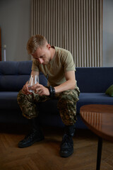 Stressed young soldier drinking water and suffering from PTSD at home