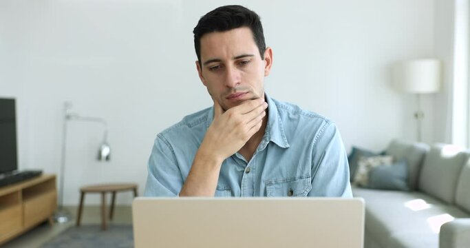 Serious Hispanic man sit at desk working on laptop, stuck with complicated task, feels perplexed due to new program, experiences lack creative ideas, looks puzzled and doubtful. Dilemma, challenge