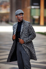 Portrait African American young male in trendy outfit coat with animal print, turtleneck, cap,...