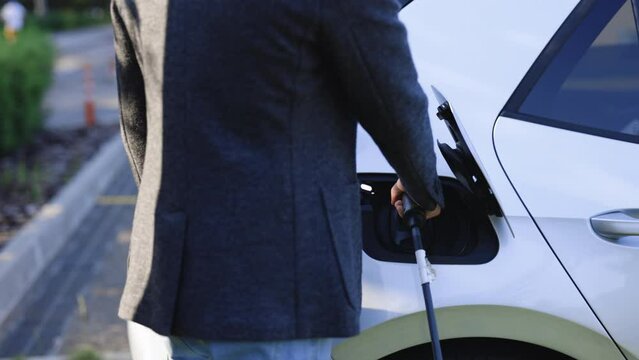 Businessman plugging electric car from charging station. Senior plugging in power cord to electric car. Male hand attaching power cable to environmentally friendly zero emission electric car