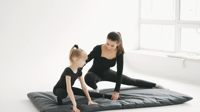 Young woman trainer and little kid practices gymnastic at studio