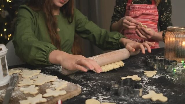 Young girl rolling dough for homemade gingerbread beside little sister at home