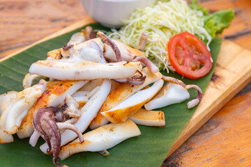 Sliced grilled squid serving with shredded cabbage and tomato.