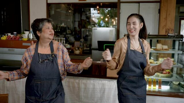 Retired mother and Asian daughter Standing to pay in front of the coffee shop, which is their own bakery. Mother and daughter dancing in front of the counter in a good mood that sells well