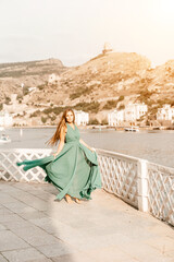 Woman sea trevel green dress. Side view a happy woman with long hair in a long mint dress posing on a beach with calm sea bokeh lights on sunny day. Girl on the nature on blue sky background.