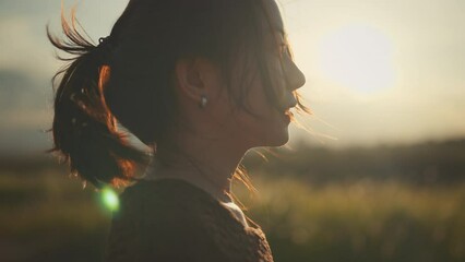 Close up portrait of Asian woman enjoying peaceful sunset. Wind blowing on hair, slow motion.