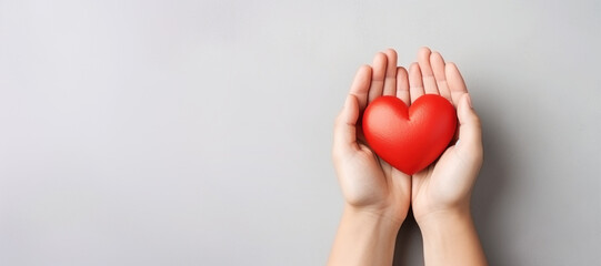 Hands holding a red heart on a gray background with copy space.
