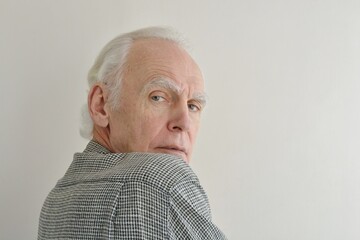 Portrait of an elderly dissatisfied gray-haired man looking over his shoulder