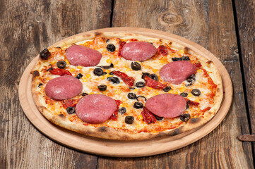 Studio shot of a hand made pizza with pepperoni, dired tomatoes and olives on beautiful weathered wooden table