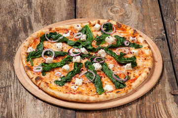 Studio shot of a hand made pizza with spinach, red onion slices and feta cheese on beautiful weathered wooden table