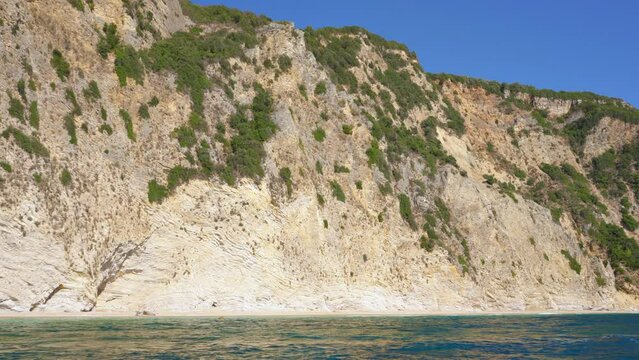 Rock geology layers visible at cliffs near Chomi or Paradise beach at Liapades, Greece, calm green sea in foreground. View from a boat
