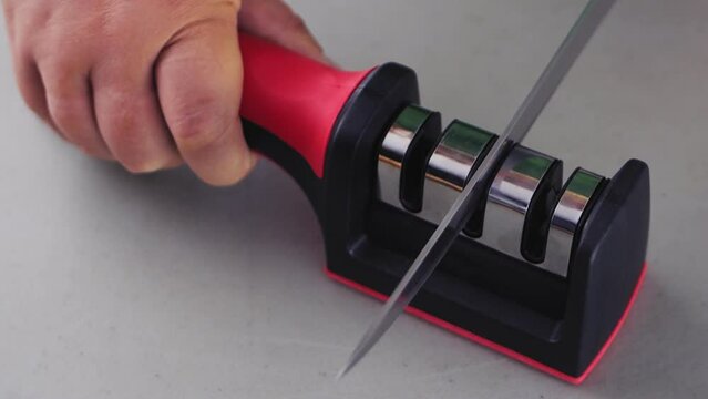 A woman's hand sharpens a kitchen knife in a knife sharpener on the table. Slowmotion
