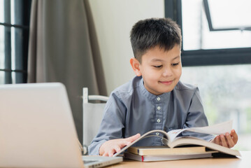 Little Asian boy student reading the book for learning. Educational concept Social distancing, staying at home, presenting a modern educational way of life.