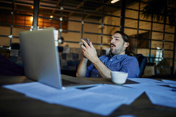 Young Caucasian man using a smartphone while working in a startup company office