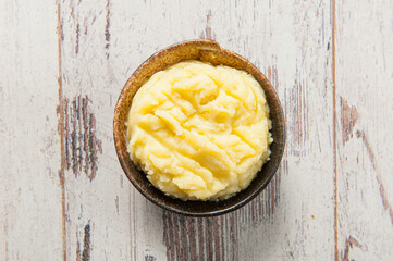 Top view of potato puree in a hand made ceramic bowl on white weathered wooden table
