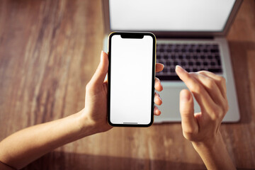 Young Caucasian woman using a smartphone and laptop with blank screens