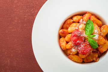 Potato gnocchi. Traditional homemade potato gnocchi with tomato sauce, basil and parmesan cheese on kitchen table on red kitchen table background. Traditional Italian food. Top view.