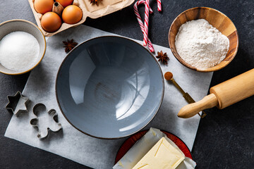 baking, cooking and christmas concept - close up of ceramic bowl, molds, rolling pin and ingredients on black table top