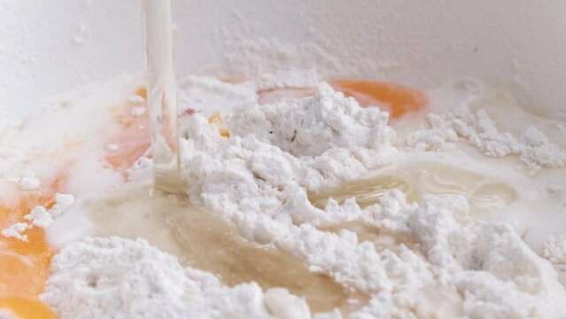 Water adding to cereal flour with egg for homemade bread preparation closeup. Mixing organic ingredients for pie bakery