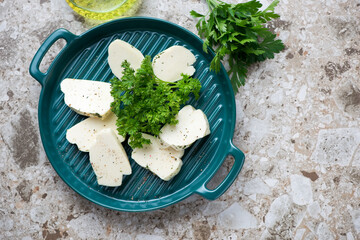 Green serving tray with sliced halloumi and fresh parsley, top view on a light-brown granite background, horizontal shot