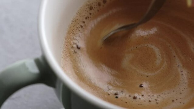 Hand stirs milk and coffee for fresh cappuccino preparation closeup. Caffeine latte hot drink with fluffy foam macro