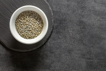 Sunflower seeds peeled kernels in  white bowl, on slate stone plate round, dark background, top view