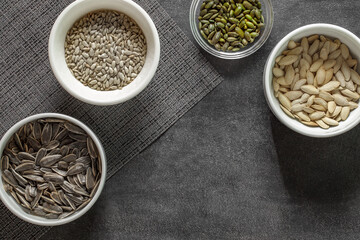 Sunflower and pumpkin seeds in bowls, on grey tablecloth on dark background, top view
