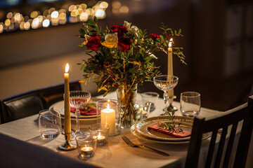 holidays, romantic date and celebration concept - close up of festive table serving for two with flowers in vase and candles burning at home on valentine's day - 645763072
