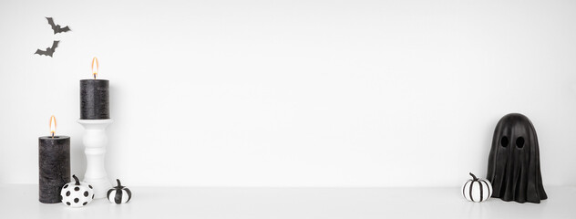 Halloween shelf decor with copy space against a white wall banner background. White shelf with black candles, pumpkins and ghost decor.