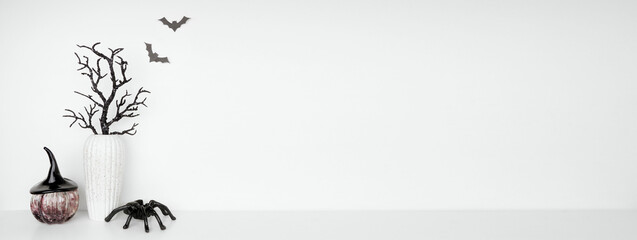 Halloween shelf decor with copy space against a white wall banner background. White shelf with pumpkin and witches hat, spooky branches and spider decor.