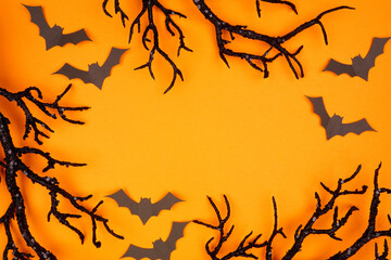 Halloween frame of spooky bats and black branches. Top view over an orange background with copy space.