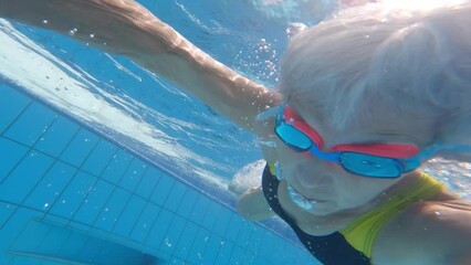 Senior woman diving in a swimming pool and shooting selfie - Powered by Adobe