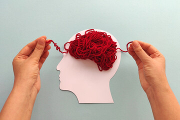 Mental health and problems with memory. Hands unraveling tangled red threads on head silhouette...