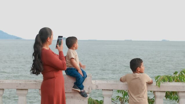 mom recording her son with her cell phone while saying hello, Latin family on vacation, long shot
