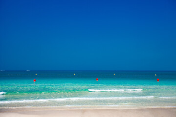 Sea with clear blue water and buoys on surface on clear sunny day, sand beach