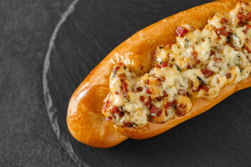 Baguette pizza with cheese and salami, on slate stone plate round, dark background, selective focus