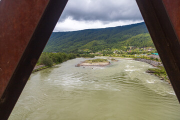 View of a river flowing in a valley surrounded by greenery with clouds over mountains in Bhutan.