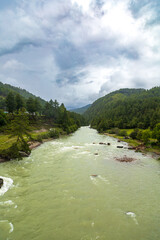 View of a river flowing in a valley surrounded by greenery with clouds over mountains in Bhutan