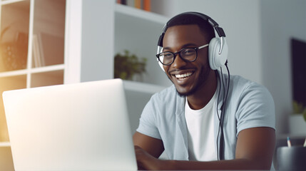 Fototapeta na wymiar Dressed in a contented smile, a young African American man with glasses and headphones is seated at his laptop,