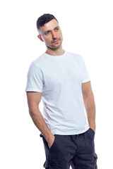 Fototapeta premium A handsome young man in a white T-shirt stands with his hands in his pockets. Isolated on a white background. Vertical.