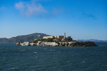 Fototapeta na wymiar Alcatraz Island in San Francisco Bay seen from ship during Harbor Cruise from SFO tourist landmark travel destination on sunny day with clouds and blue sky